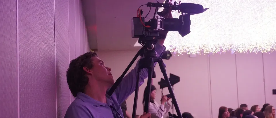 Mitchell Carlyle operating a cinema camera on a tripod at an evening event